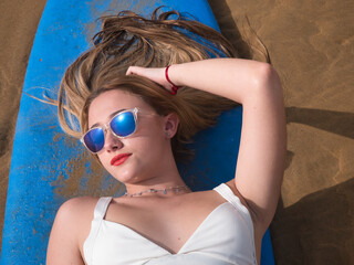 Portrait of young woman, blonde and beautiful, with a white bikini and sunglasses, lying on a blue...