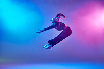 Naklejka na ściany i meble a girl in dark clothes dances on a neon background in smoke, modern dance