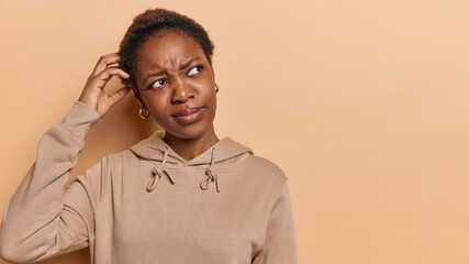 Doubt need to think. Dark skinned woman has puzzled expression scratches head has confused face...
