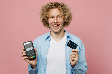 Young blond man wear blue shirt white t-shirt hold wireless modern bank payment terminal process acquire credit card isolated on plain pastel light pink background studio portrait. Lifestyle concept