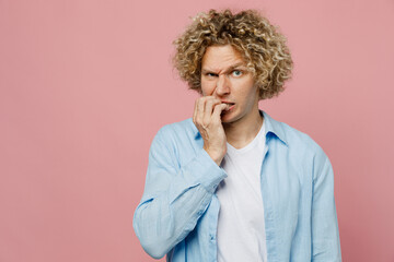 Fototapeta na wymiar Young sad minded pensive thougthful caucasian blond man wear blue shirt white t-shirt look camera biting nails fingers isolated on plain pastel light pink background studio portrait Lifestyle concept