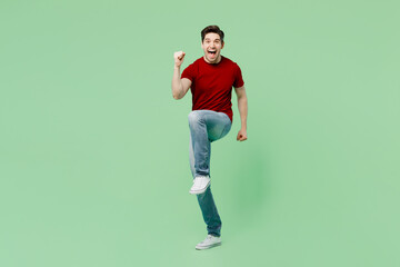 Full body young brunet man he wears red t-shirt casual clothes doing winner gesture celebrate clenching fists say yes isolated on plain pastel light green background studio portrait Lifestyle concept