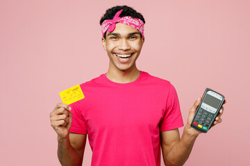 Young man of African American ethnicity wear headscarf t-shirt casual clothes hold wireless bank payment terminal to process acquire credit card isolated on pastel plain light pink color background.