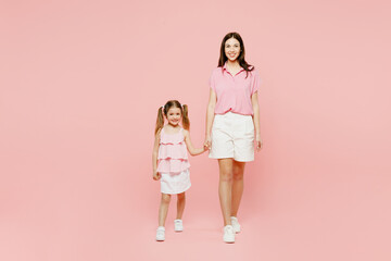 Full body smiling woman wear casual clothes with child kid girl 6-7 years old. Mother daughter look camera hold hands walk together isolated on plain pastel pink background. Family parent day concept.