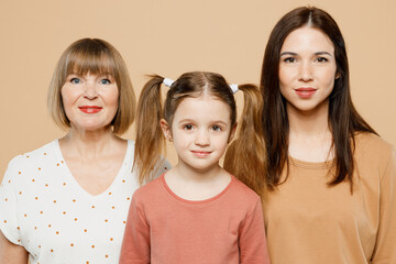 Close up happy caucasian fun lovely women wearing casual clothes with child kid girl 6-7 years old. Granny mother daughter looking camera isolated on plain beige background. Family parent day concept.