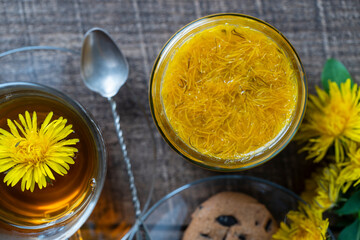 Sweet jam from ripe yellow petals of dandelion flowers, orange, lemon and sugar on the wooden table with tea and cookies, top view, closeup