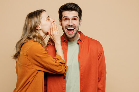 Young couple two friend family man woman wear casual clothes whisper gossip and tell secret behind her hand sharing news together isolated on pastel plain light beige color background studio portrait