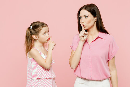 Happy woman wear casual clothes with child kid girl 6-7 years old. Mother daughter say hush be quiet, finger on lips shhh gesture isolated on plain pastel pink background. Family parent day concept.