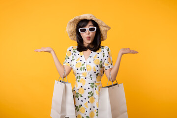 Portrait happy attractive young asian woman with trendy springtime dress, hat, sunglasses fashion and paper bag isolated on yellow background. Summertime sale shopping concept.