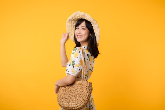 Portrait happy attractive young asian woman with trendy springtime dress, hat, sunglasses fashion and woven bag isolated on yellow background. Summertime sale shopping concept.
