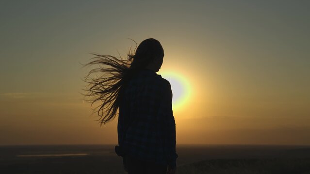 young girl looks at sunset and prays, religious person, her hair is flying in wind in glare of the sun, to believe in goodness, a woman's dream of love, to think and ask for forgiveness from heaven