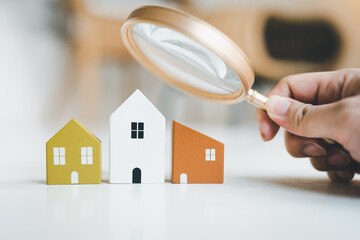 Hand holding magnifying glass and looking at house model, house selection, real estate concept.	
