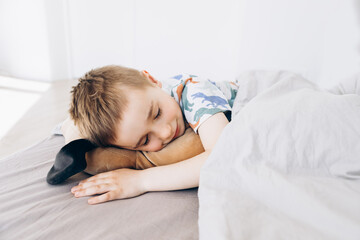 Obraz na płótnie Canvas Happy cute tired little boy lies on comfort bed with closed eyes, hugs toy dog, sleeping in bedroom interior, top view, free space, close up. Health care, childhood, rest, relax at night