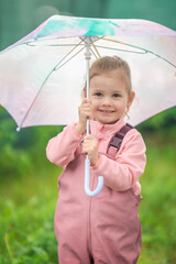 Happy laughing child girl 2-3 year old wearing waterproof clothes and holding pink umbrella have a fun on home backyard in rainy day