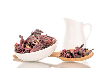 Karkade tea in white ceramic saucer with milk jug and wooden spoon, macro, isolated on white background.