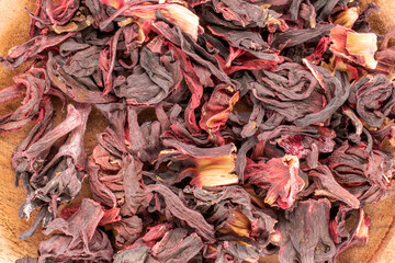 Dry fragrant karkade tea on a wooden saucer, macro, top view.