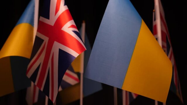 Close up of group of flags of GB UK and Ukraine against dark background moving slowly.