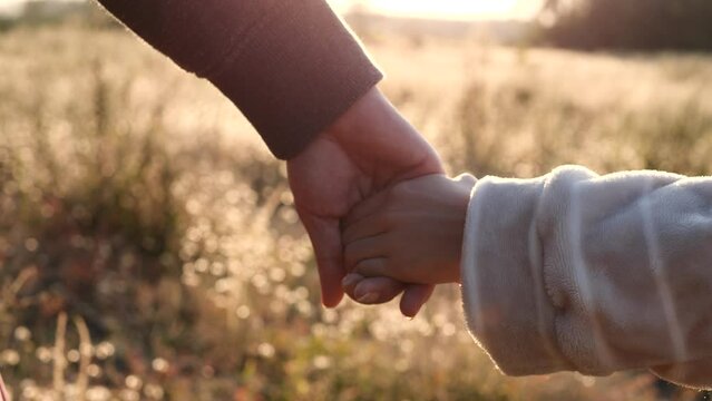Close-up of a mother and her daughter holding hands and being joined at sunset on a nature background, 4K. Happy Family, Love, Couple, Parent, Toddler, and Valentine's Day as a Concept