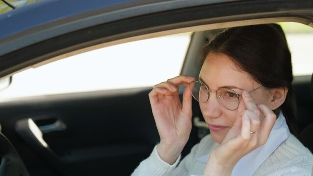 A beautiful young woman sits in a car, puts on glasses, looks at the camera and smiles. The concept of the meaning of ophthalmology for drivers