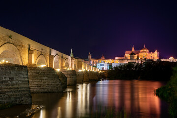 Puente Romano in Córdoba, Spain at night, long exposure with reflecting city lights.