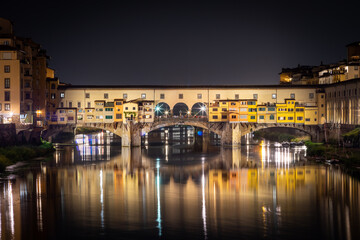 Ponte Vecchio at night. Reflections of colorful city lights in the river. Florence, Italy.