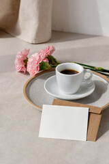 Empty paper card, coffe cup and flowers on beige background with sun light shadow, aesthetic floral holiday or wedding morning composition with mockup copy space