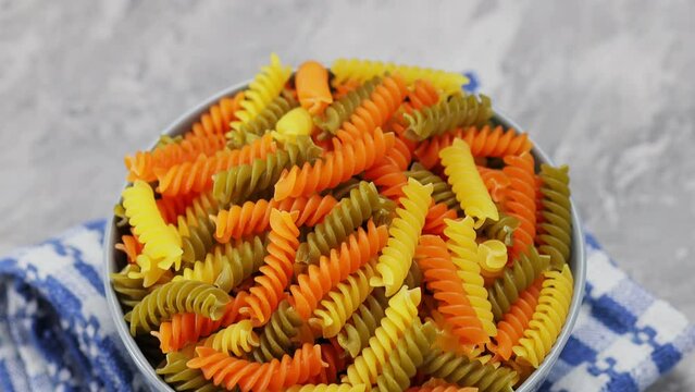 Raw colorful italian fusilli pasta on a gray background. Dry tricolor fusilli pasta in bowl. Tilt down camera movement