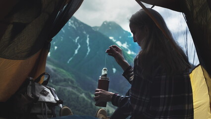Young girl hiker uses a tea bag in the mountains. Tea drinking outdoors from a thermos