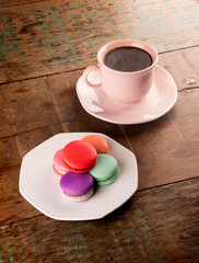 Fototapeta na wymiar colorful chocolate filled macarons in white ceramic plate on rustic wooden table.with cup of hot coffee in portrait angle