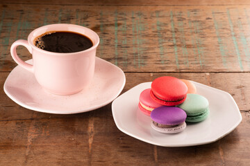 Obraz na płótnie Canvas colorful chocolate filled macarons in white ceramic plate on rustic wooden table.with a cup of hot coffee