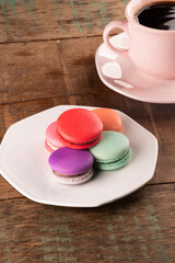 colorful chocolate filled macarons in white ceramic plate on rustic wooden table.with cup of hot coffee close-up