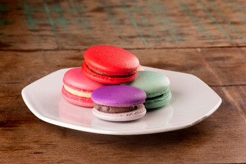 colorful macarons filled with chocolate in white ceramic plate on rustic wooden table close-up