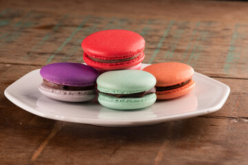 colorful chocolate filled macarons in white ceramic plate on rustic wooden table