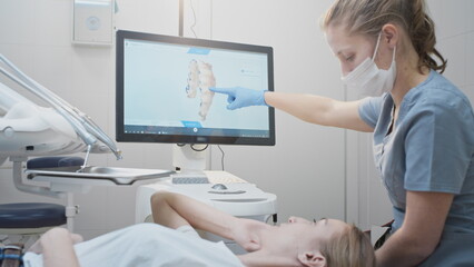 Girl doctor dentist demonstrates a 3D model of teeth on a touch monitor. Dental consultation in the...