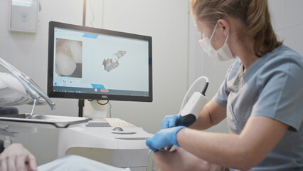 Doctor scans the patient's teeth in the clinic. The dentist holds in his hand a manual 3D scanner for the jaw and mouth. Dental health. Creates a 3D model of teeth and gums on a medical monitor