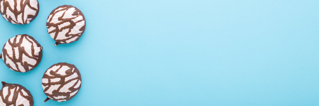 Pink soft zephyr covered with dark brown chocolate glaze on light blue table background. Pastel color. Closeup. Sweet snack. Food wide banner. Empty place for text. Top down view.