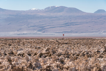 Rugged salt plains with dramatic mountains in the background and a single road sign.
