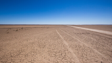 Fototapeta na wymiar Car track lines in flat desert sand as a gravel road stretches to the horizon