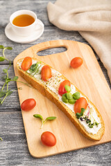Long white bread sandwich with cream cheese, tomatoes and microgreen on gray. side view, selective focus.