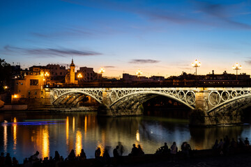 Fototapeta premium Torre Sevilla and Puente de Isabel II reflected in the river Guadalquivor during blue hour. Sevilla, Spain.