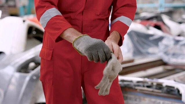 Close-up hands car mechanic caucasian man, wear work clothes in large garage protect from dirt work safety, mechanic is picking up glove putting it on hand before starting repair car.
