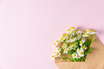 White chamomile flowers bouquet in envelope on pastel pink background. Mothers day or wedding card. Top view