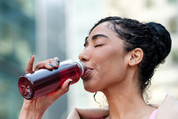 Headshot of fitness young woman drinking energy drink outdoors.