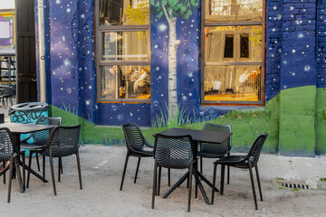 Fototapeta na wymiar Black cafe chairs and tables next to reative drawing building and cafe
