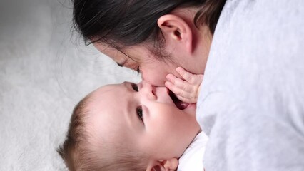baby boy adorable newborn infant lying on bed looking up.mother kissing kid cheek,tenderness,caresses.toddler is talking something moving lips,close up face portrait 4k.woman hand on body, tongue out