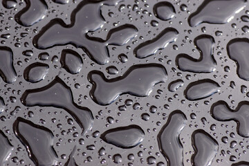 Close up of the texture of rainwater, raindrops on a black glass table with scratches. Pattern