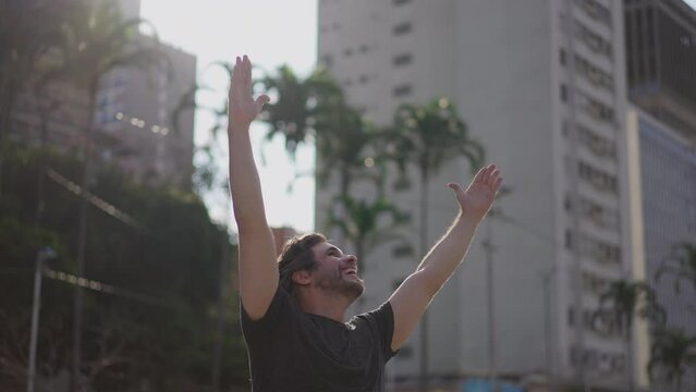 One contemplative happy young man cheering success while standing outdoors raising arms in the air feeling happiness and gratitude