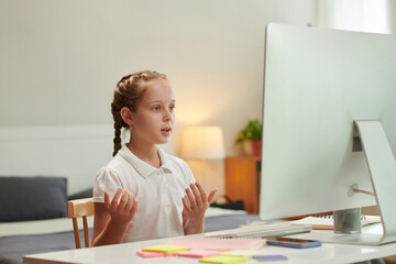 Schoolgirl speaking in front of computer when attending online class