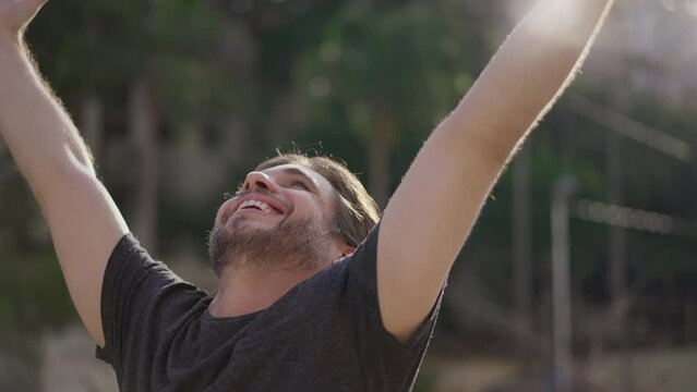 One ecstatic young man with arms raised upwards having HOPE and FAITH. Person celebrates success looking up smiling while standing outdoors at park sunlight