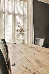 a dining table and chairs in a room with white blinds on the window behind it is a vase of flowers